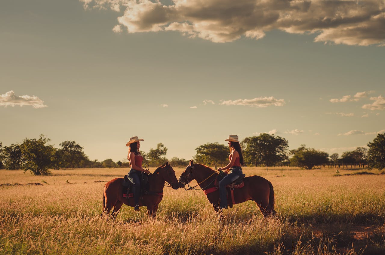 Two women horseback riding in a sunny Brazilian field during sunset, showcasing nature's serenity.
